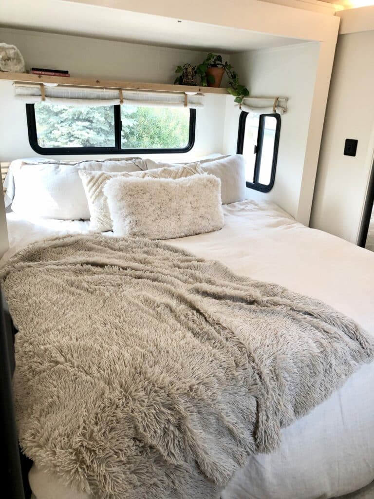 Natural wood shelf above an RV bed replacing a bulky overhead cabinet